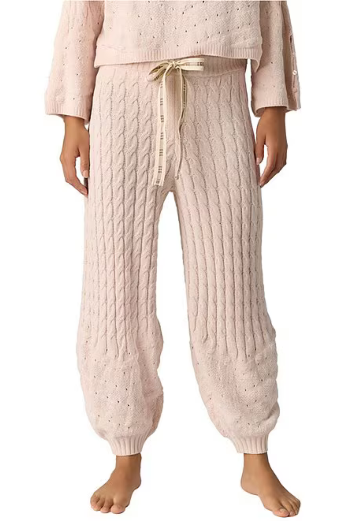 A person wearing light blush pink cable-knit harem pants with a cream drawstring and a matching knit top, shown against a plain white background.