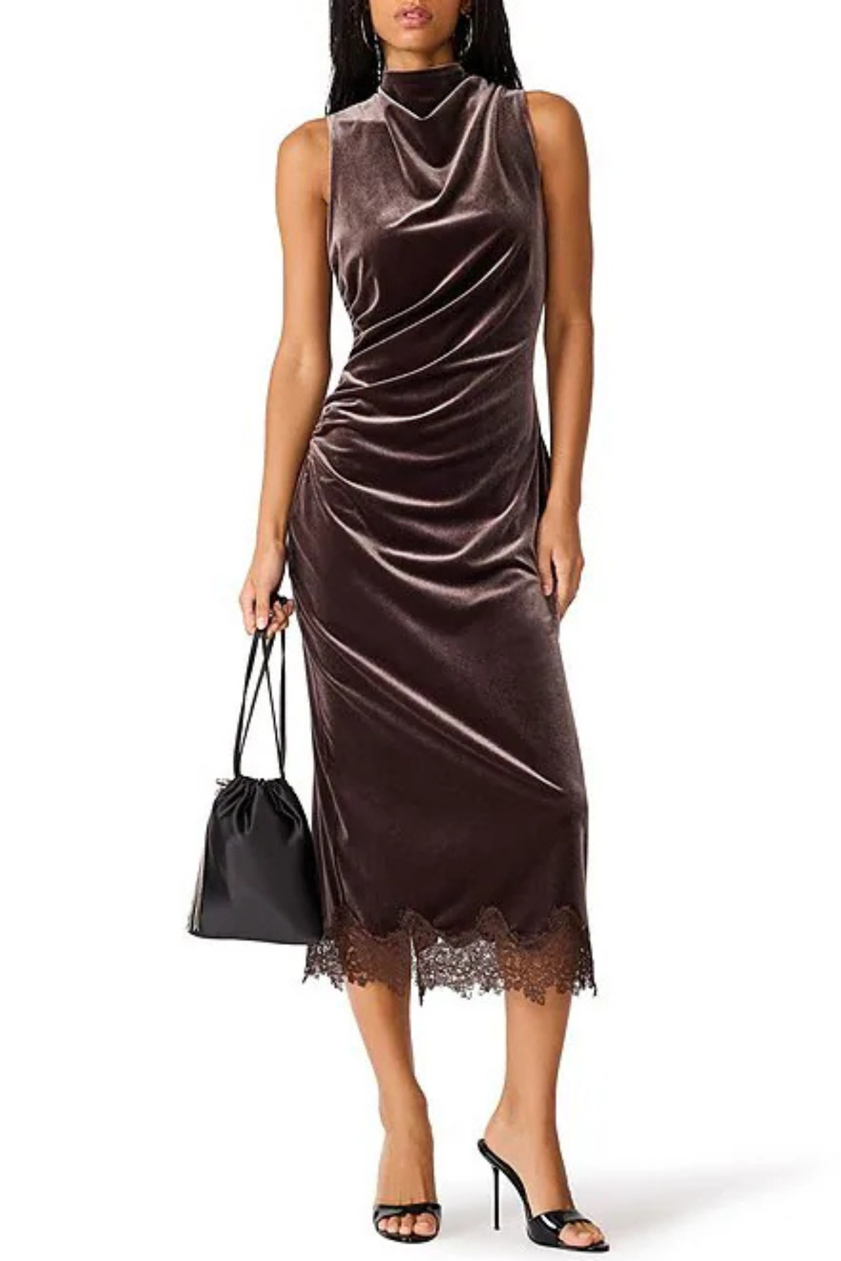 A woman modeling a sleeveless, high-neck midi dress in dark brown velvet with a lace hem, holding a black handbag against a plain white background.