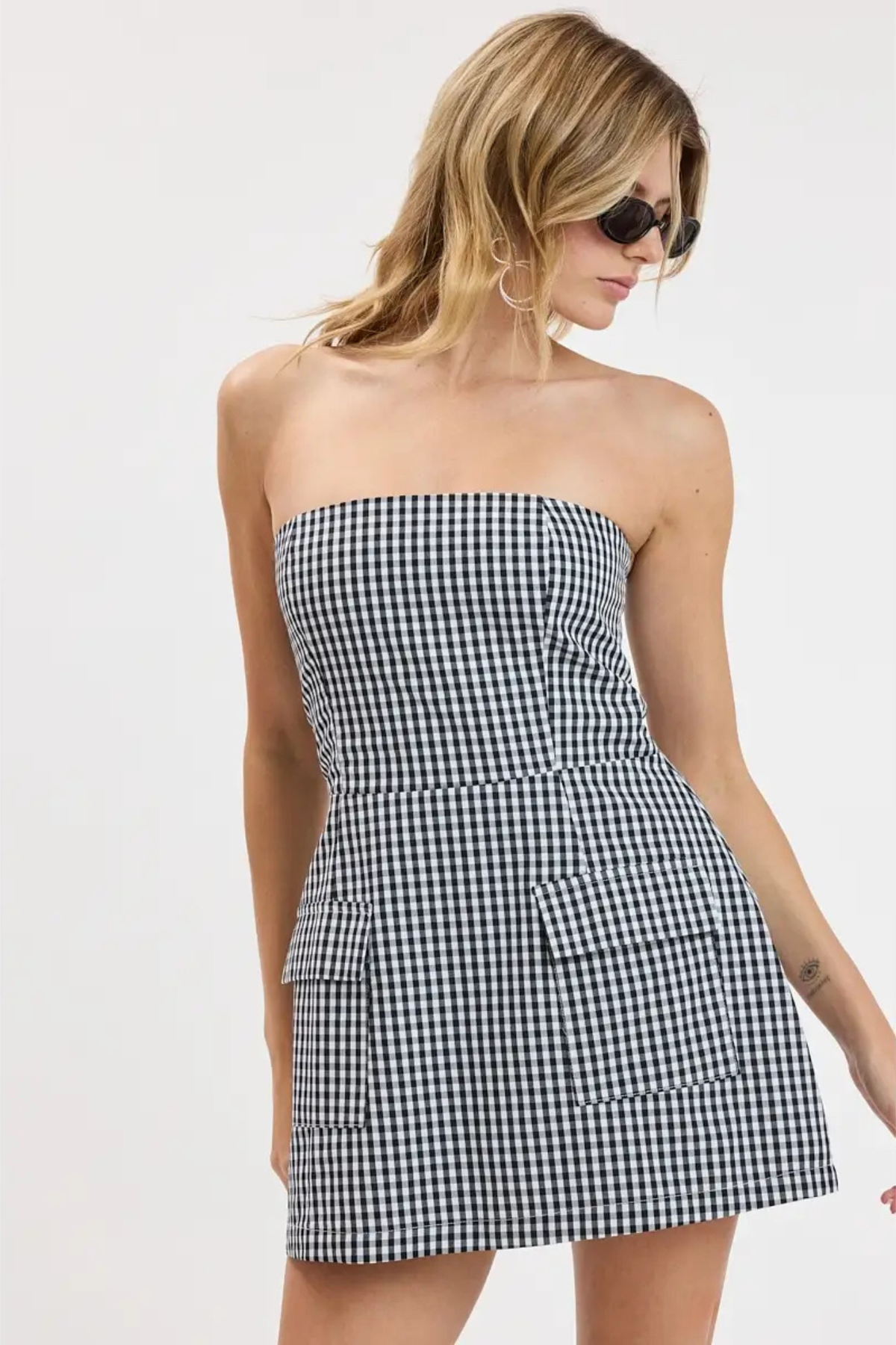 A woman modeling a strapless black and white gingham mini dress against a plain white studio background.