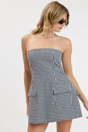 A woman modeling a strapless black and white gingham mini dress against a plain white studio background.