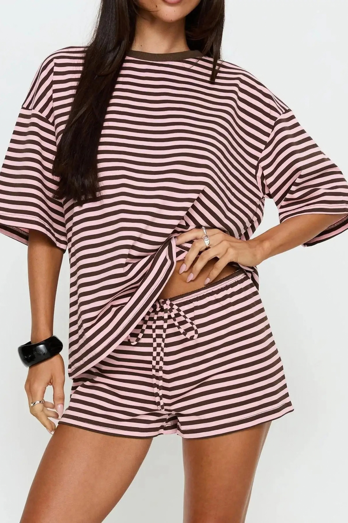 A woman wearing a matching two-piece lounge set with wide-sleeve top and drawstring shorts, both featuring dark brown horizontal stripes on a light pinkish-beige base, against a plain light gray background.