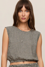 A woman wearing a sleeveless black and white gingham crop top against a plain beige background.