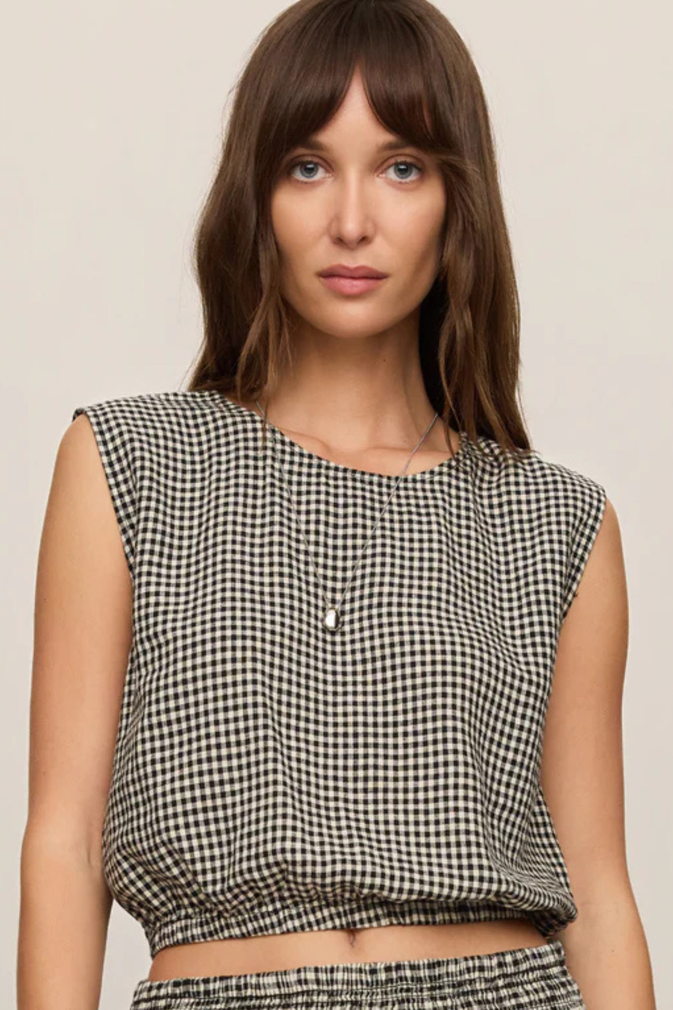 A woman wearing a sleeveless black and white gingham crop top against a plain beige background.