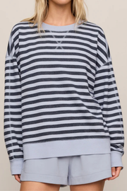 A woman wearing a navy and light gray striped long-sleeve sweatshirt with matching light gray shorts, shown from the neck to the upper thighs against a plain beige studio background.