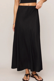 A black maxi skirt worn by a model, shown from the waist down against a plain light gray studio background.