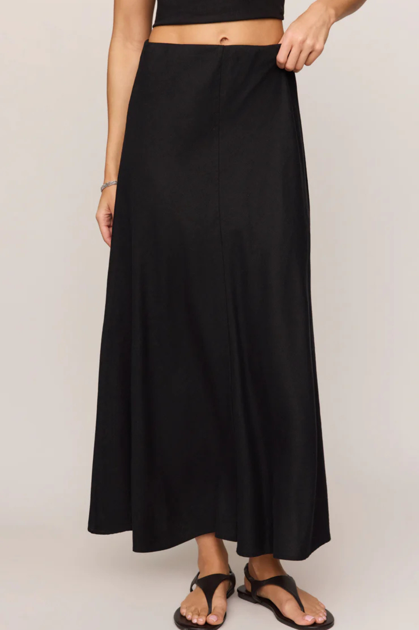 A black maxi skirt worn by a model, shown from the waist down against a plain light gray studio background.