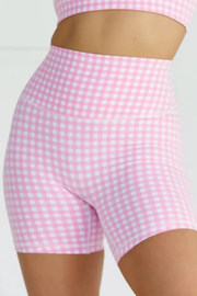 Pink and white gingham check high-waisted athletic shorts shown on a model, with a matching pink crop top partially visible at the top.