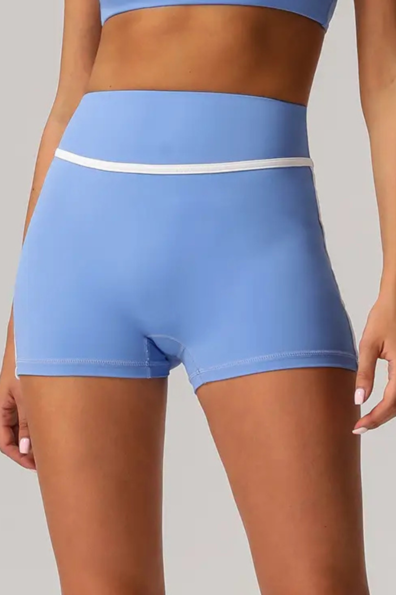 Light blue athletic shorts with a white waistband stripe, shown on a model from the waist to upper thighs against a plain light gray studio background.
