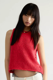 A model wearing a vibrant red sleeveless knit top with a crew neck and side buttons, paired with white pants, against a plain light gray background.