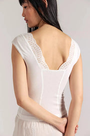 Woman wearing a white sleeveless top with lace details on a plain background