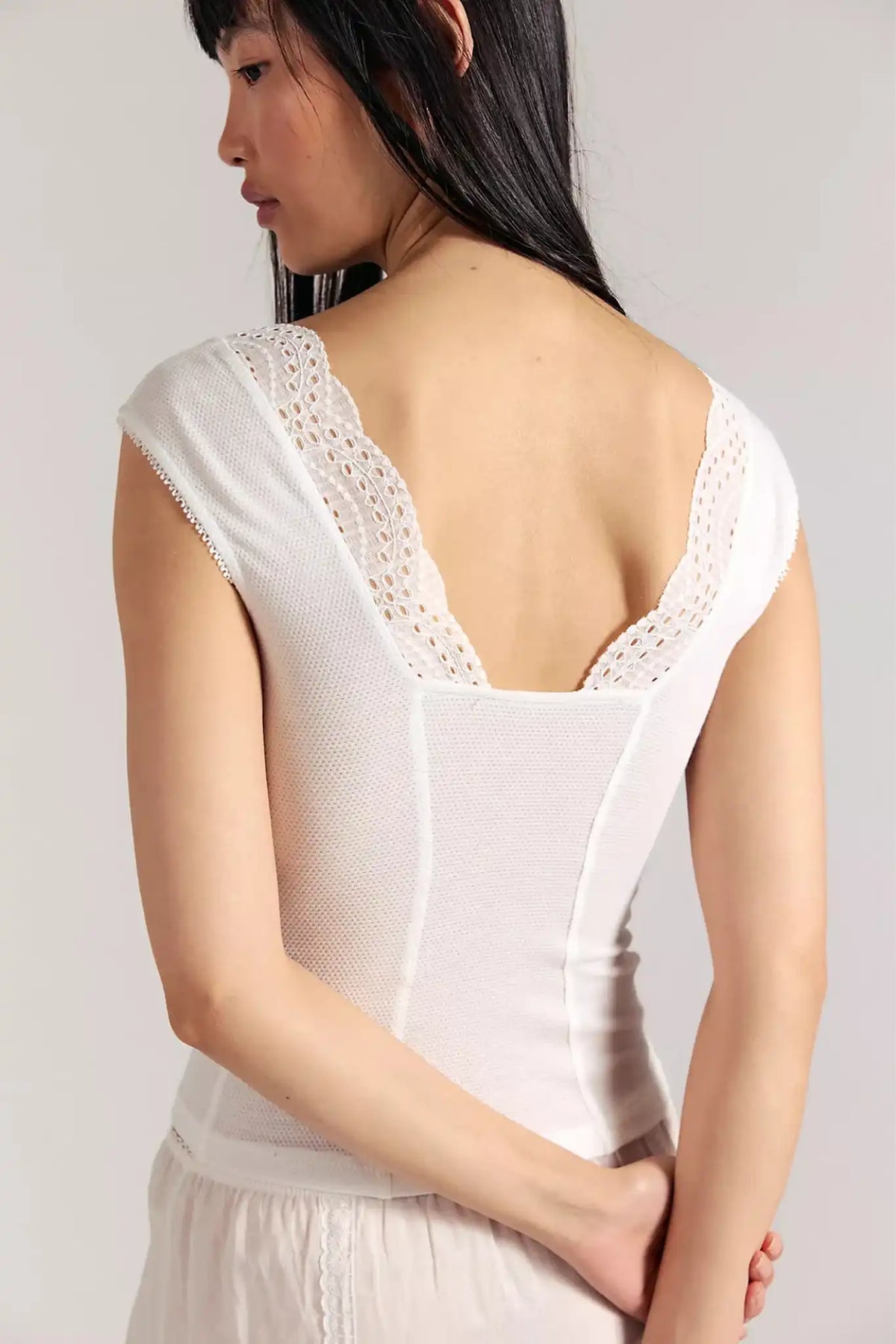 Woman wearing a white sleeveless top with lace details on a plain background