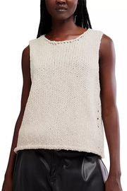 A sleeveless knit top in a warm off-white or cream color, featuring a textured open-knit pattern and a scalloped trim along the neckline, worn by a model with black leather pants against a white background.