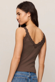 A woman shown from the back wearing a brown ribbed tank top with dark lace trim along the open back neckline, paired with blue jeans, against a plain light beige studio background.