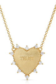 A gold heart-shaped pendant necklace with the word 'TRUST' engraved in the center, surrounded by small clear gemstones along the edge, on a white background.