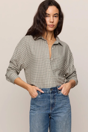 A woman wearing a long-sleeve button-up shirt with a beige and gray gingham pattern, paired with blue jeans, standing against a plain light beige background.