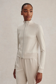 A model wearing a cream-colored ribbed knit zip-up jacket and matching knit pants against a neutral beige background.