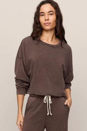 A woman modeling a dark brown washed crewneck sweatshirt and matching brown sweatpants against a light gray studio background.