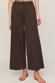 A model wearing dark brown wide-leg cropped pants and tan strappy flat sandals, shown from the waist down against a light beige studio background.
