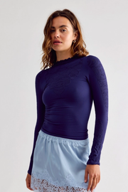 A woman modeling a dark navy blue long-sleeve top with lace detailing on the shoulders and sleeves, paired with a light blue skirt, against a plain light gray background.