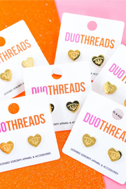 Five white DUOTHREADS display cards, each holding two small heart-shaped gold-tone jewelry pieces, arranged on a glittery orange and pink background. The cards feature the DUOTHREADS logo in orange and pink, and the jewelry appears to be candy cane or heart-shaped accessories with 'CUPID' or similar text inside.
