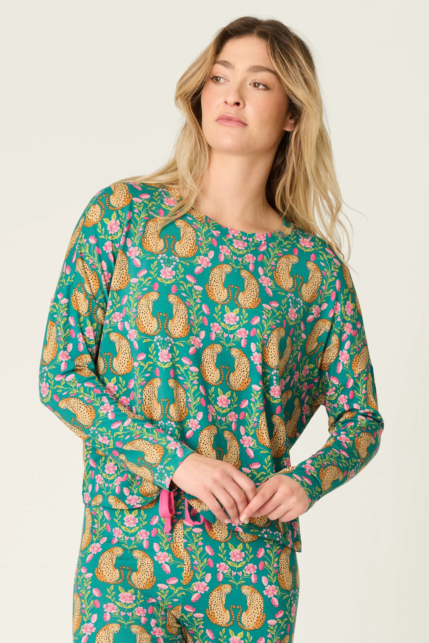 A woman wearing a long-sleeve pajama top with a green base and a colorful paisley and floral print, paired with matching pants, against a plain light background.