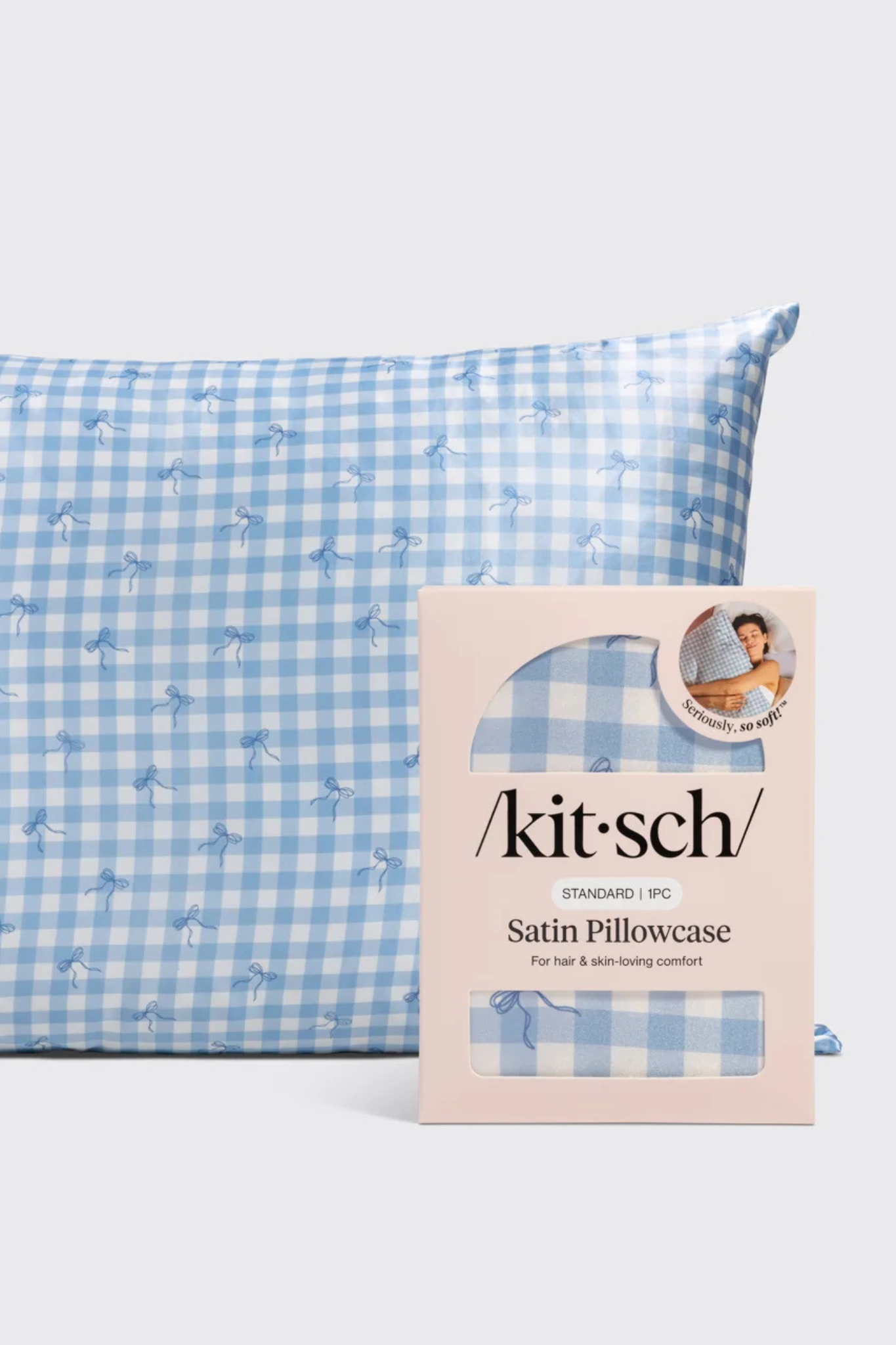 A light blue and white gingham satin pillowcase with a small dalmatian print, shown next to its pink Kit-Sch retail packaging box.
