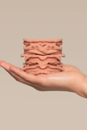A hand holding a small stack of wavy, peach-colored silicone or rubber pads against a plain beige background.