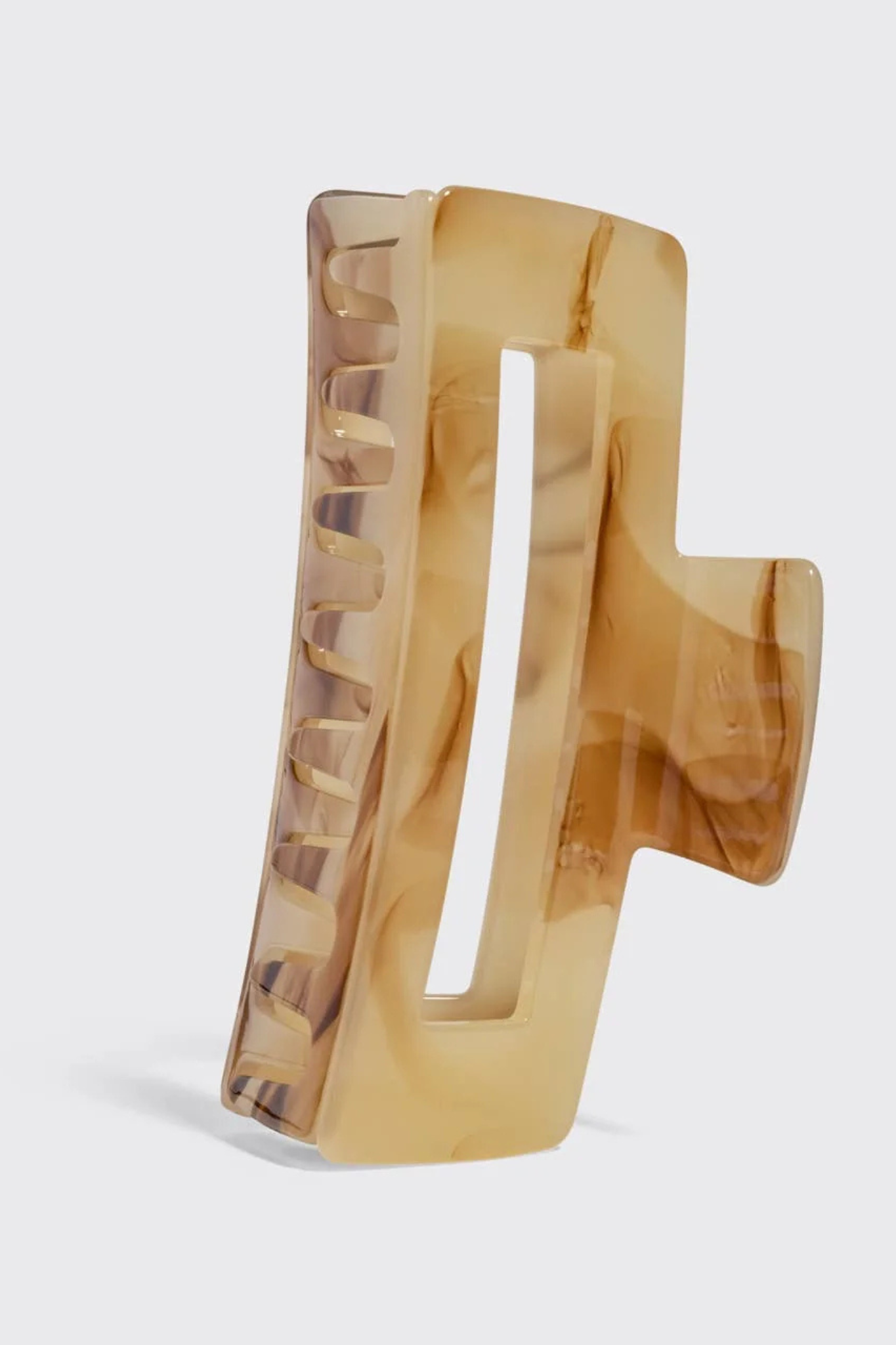 A large rectangular hair claw clip made of translucent amber acetate with natural marbled swirls, shown standing upright on a light gray background.