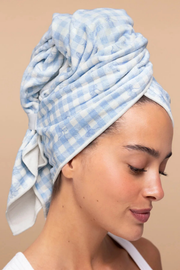 A woman wearing a light blue and white gingham checkered cotton towel wrapped around her head, shown in profile against a solid beige background.