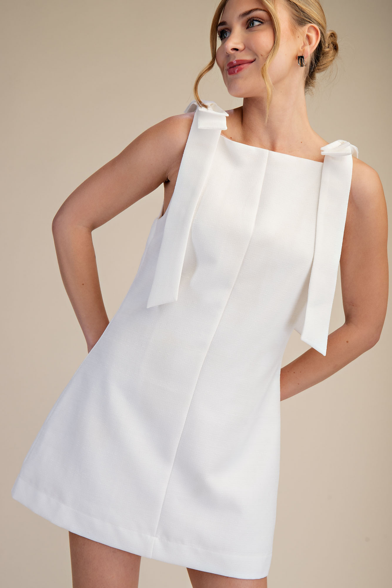 Woman wearing a white dress with bow straps against a beige background