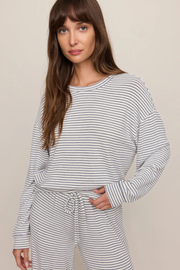 A woman wearing a matching long-sleeve striped lounge set with a crew neck top and drawstring pants, photographed against a plain beige studio background.