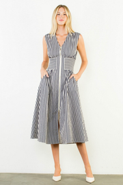 A woman modeling a sleeveless midi dress with vertical black and white stripes, standing against a plain white wall.