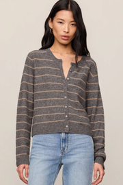A woman wearing a gray and brown striped knit henley cardigan with light blue jeans, photographed against a plain beige studio background.