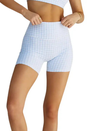 A model wearing light blue and white gingham check high-waisted biker shorts, shown from the waist to the upper thighs against a plain white background.
