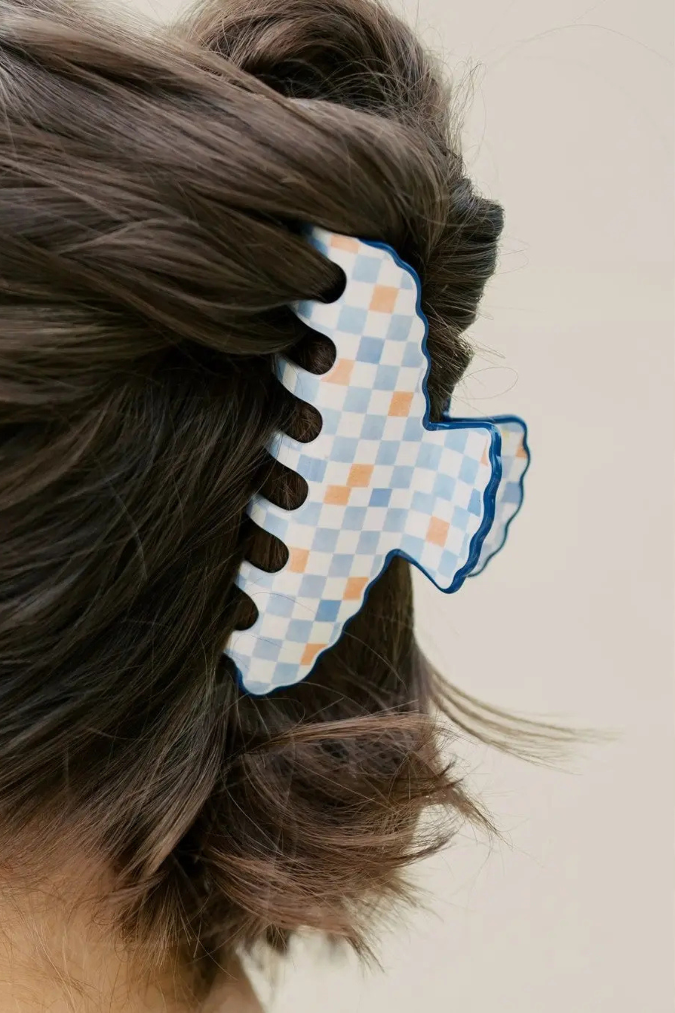 A close-up of a person's brown hair secured with a large, scalloped claw hair clip featuring a light blue and white checkered pattern with a blue border.