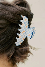 A close-up of a person's brown hair secured with a large, scalloped claw hair clip featuring a light blue and white checkered pattern with a blue border.