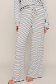 A person wearing loose, wide-leg pajama pants with thin gray horizontal stripes on a white base, shown from the waist down against a plain beige studio background.