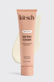 A tube of Akit-Sch smoothing Air Dry Cream in a soft peach-pink color, displayed against a light gray background with a cream-colored smear graphic behind it.