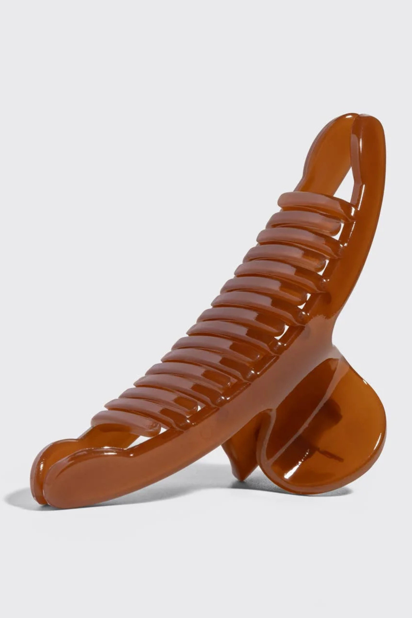 A glossy, translucent brown hair claw clip with a ribbed textured grip, shown on a light gray background.
