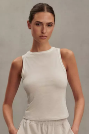 A woman modeling a sleeveless cream-colored ribbed tank top against a neutral gray studio background.