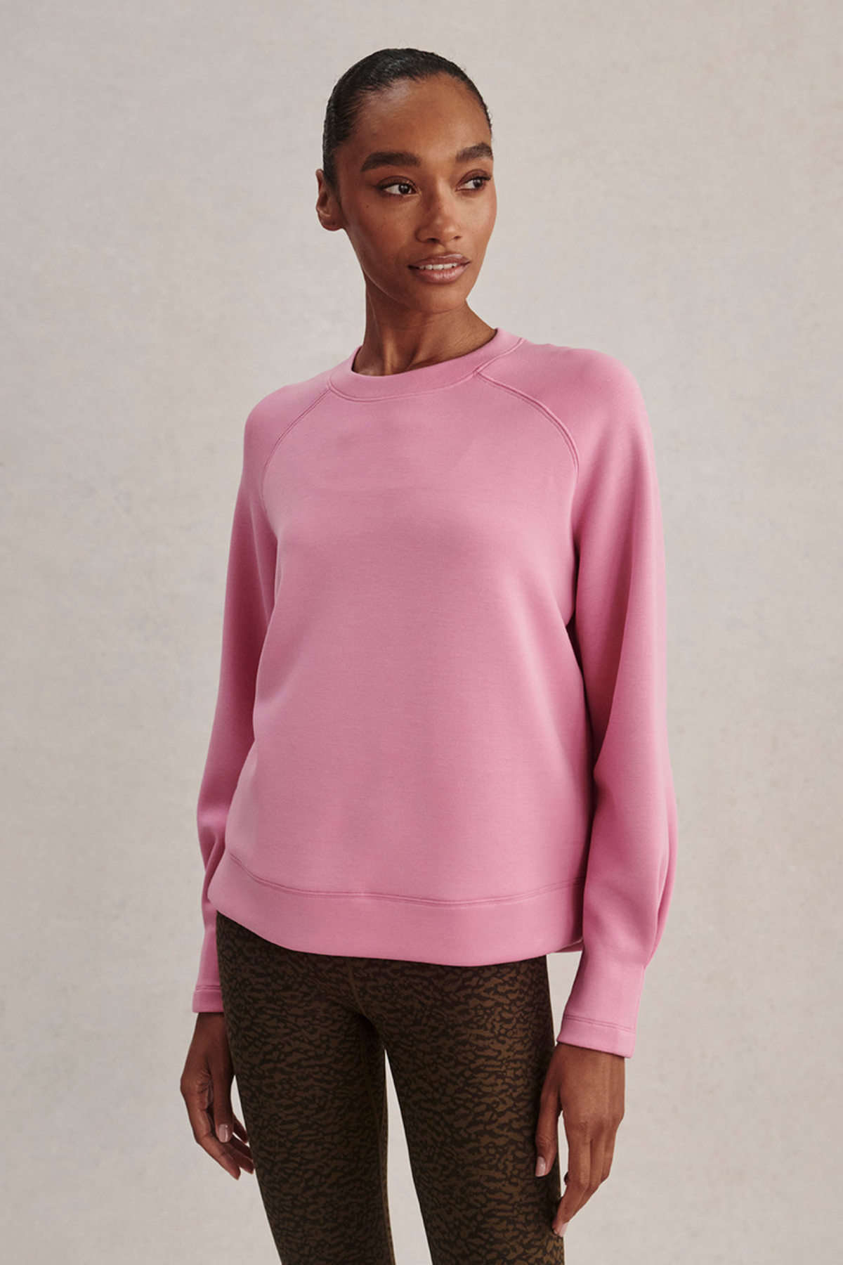 A woman modeling a dusty pink long-sleeve crewneck sweatshirt, paired with brown leopard-print leggings, against a neutral beige textured background.