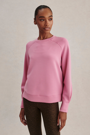A woman modeling a dusty pink long-sleeve crewneck sweatshirt, paired with brown leopard-print leggings, against a neutral beige textured background.