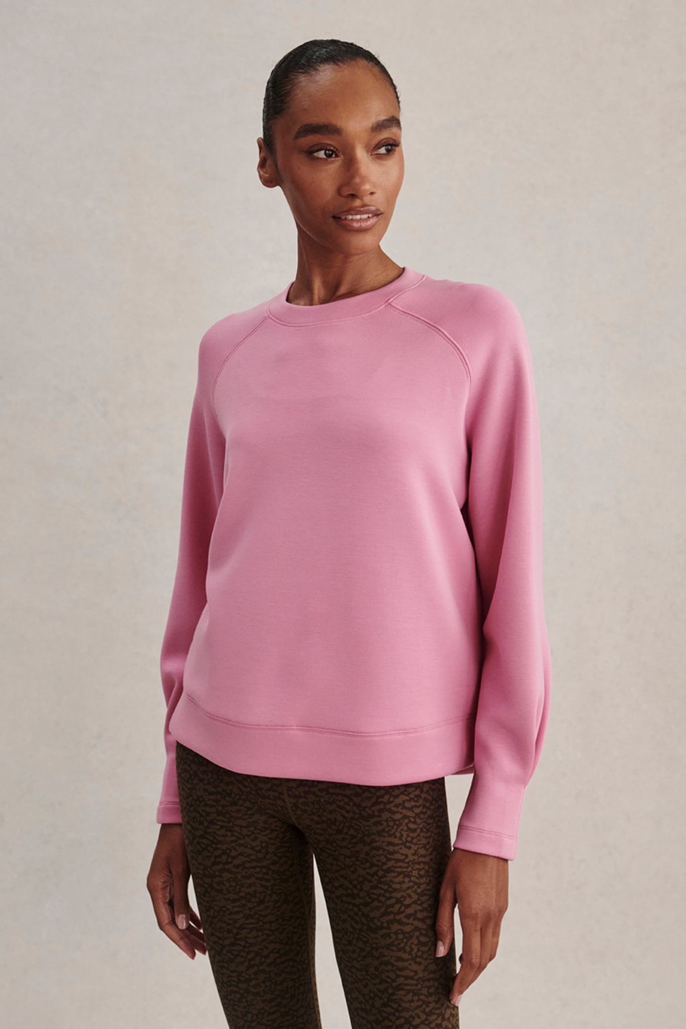 A woman modeling a dusty pink long-sleeve crewneck sweatshirt, paired with brown leopard-print leggings, against a neutral beige textured background.