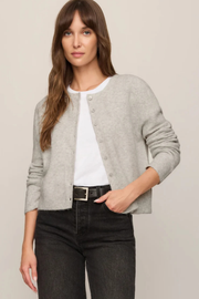 A woman modeling a light gray button-front cardigan over a white top and black jeans, photographed against a plain light beige studio background.