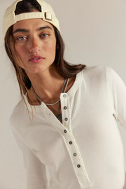 Person wearing a beige cap and white shirt with black buttons on a plain background