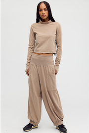 A model wearing a matching beige two-piece loungewear set, consisting of a long-sleeve cropped mock neck top and wide-leg jogger pants, paired with black sneakers, against a plain light gray background.