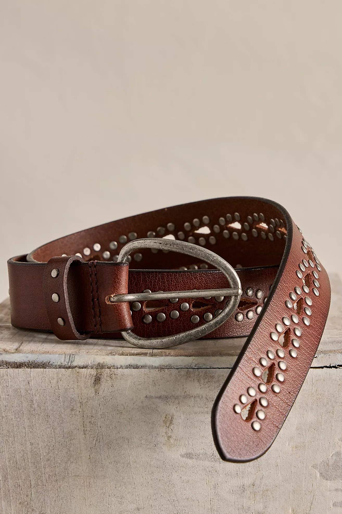 Brown leather belt with studded details on a stone surface
