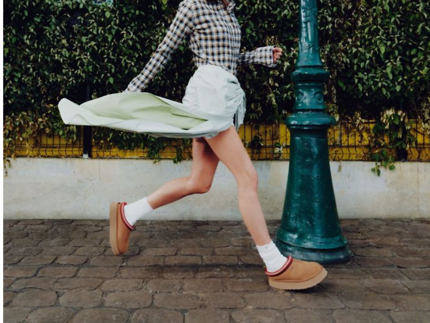 Person walking on a sidewalk with a green lamp post and foliage in the background
