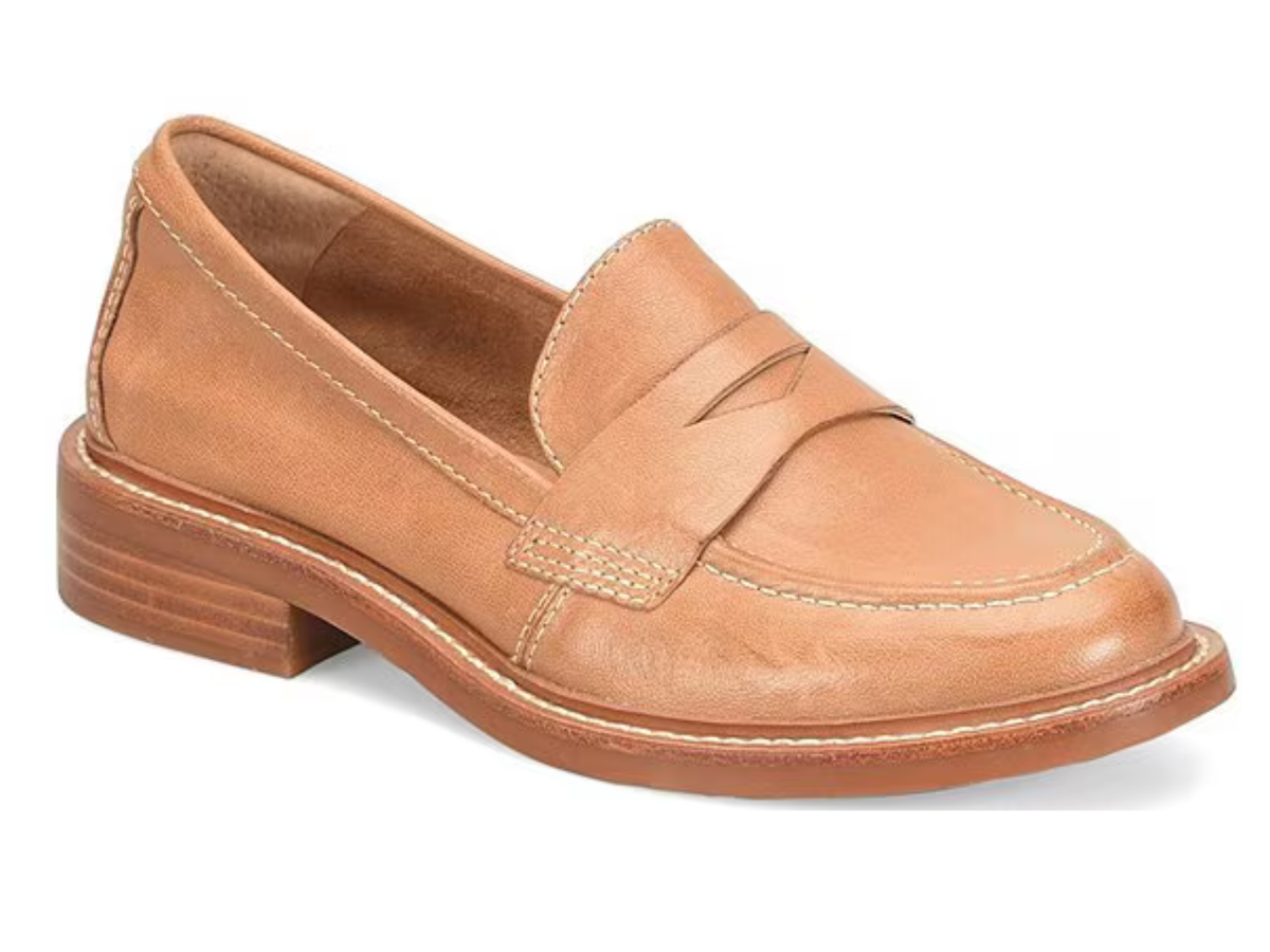 A tan leather penny loafer with a low stacked heel, photographed from a three-quarters angle on a white background.