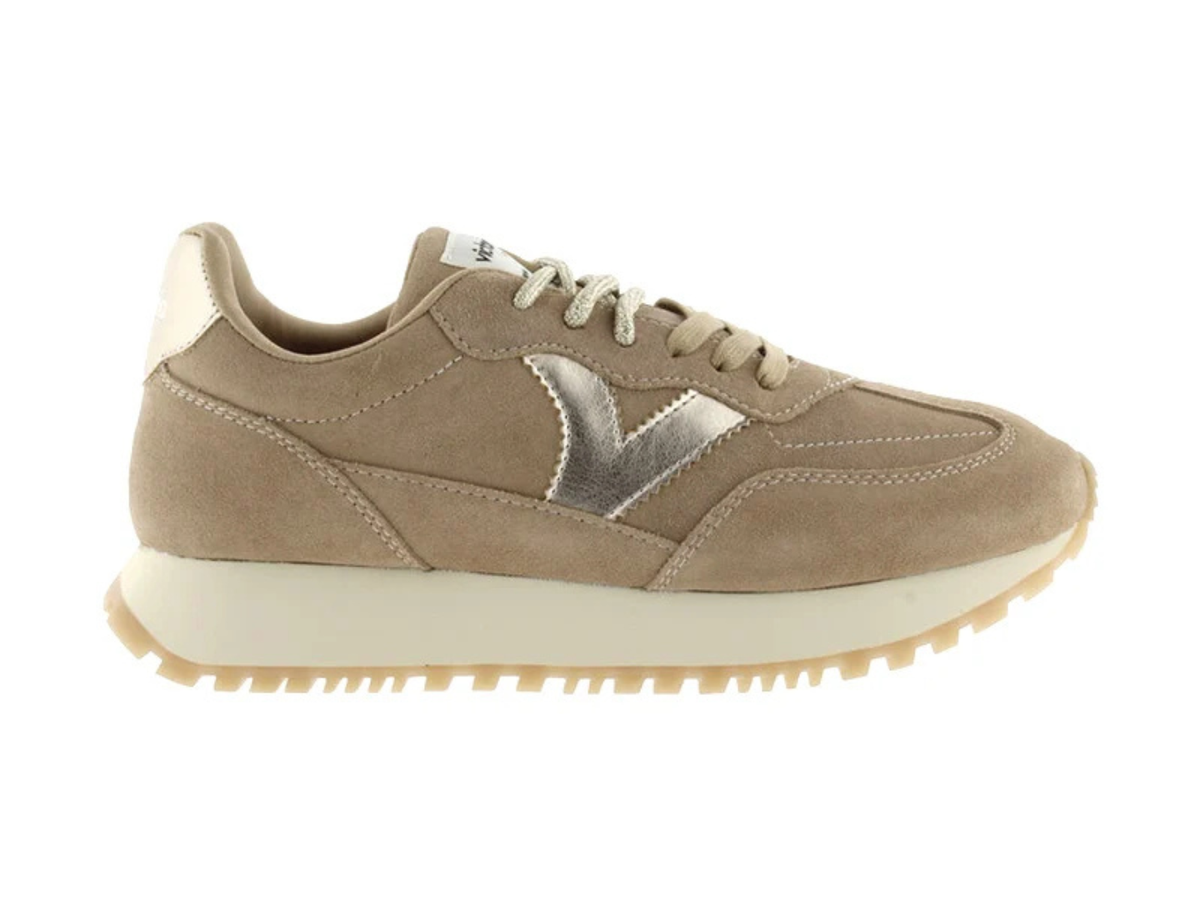 A taupe suede sneaker with a metallic silver chevron logo on the side, cream laces, and a thick cream midsole with a gum outsole, shown in profile against a white background.